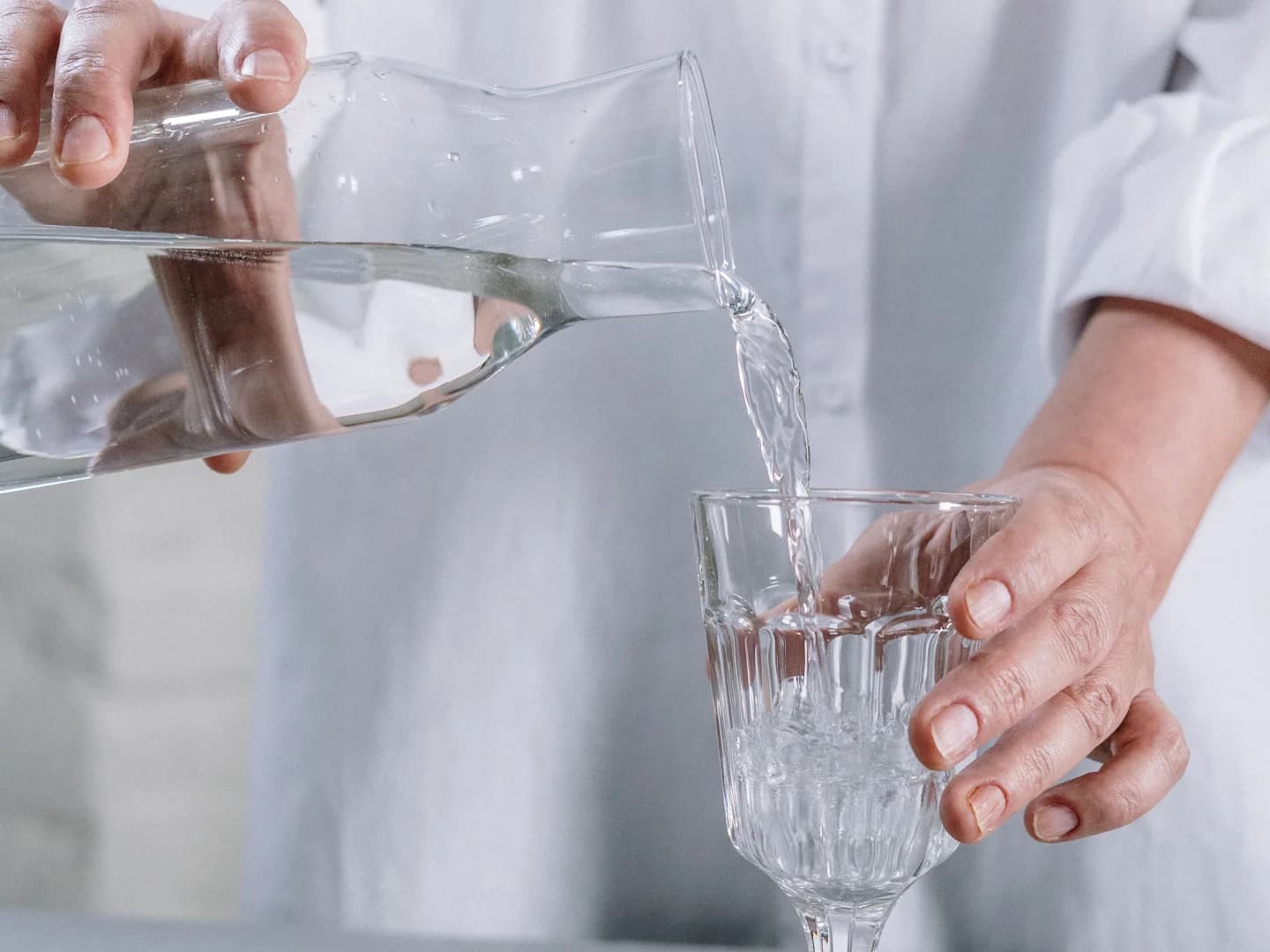 Hands pour water from a clear pitcher into a glass